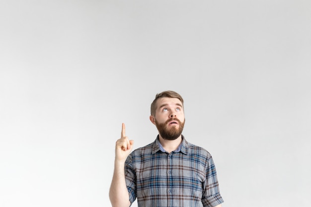 Homem jovem hippie surpreso com um bigode, posando em um fundo branco em surpresa, apontando para cima. surpresa e um local para publicidade e links.