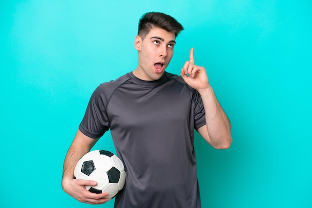 Foto homem jovem jogador de futebol caucasiano isolado em fundo azul pensando em uma ideia apontando o dedo para cima