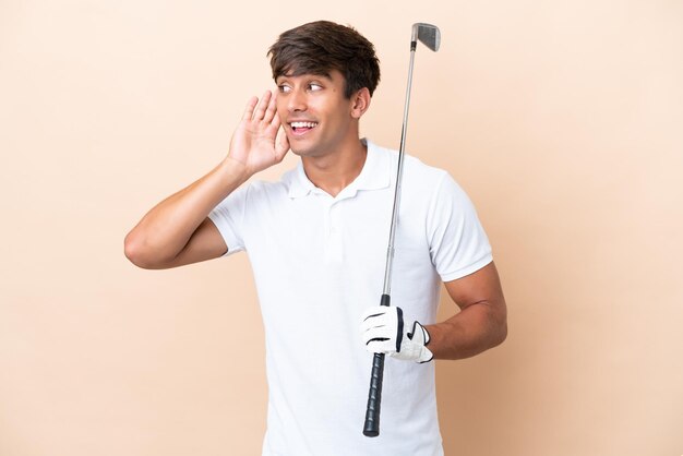 Homem jovem jogador de golfe isolado em fundo ocre, ouvindo algo, colocando a mão na orelha