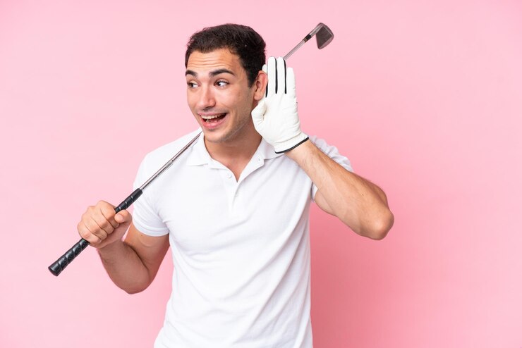 Foto homem jovem jogador de golfe isolado em fundo rosa ouvindo algo colocando a mão na orelha