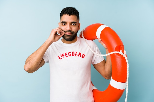 Homem jovem latino salva-vidas isolado com os dedos nos lábios, mantendo um segredo.