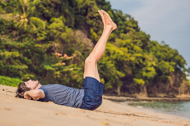 Homem jovem malhando na praia, homem esportivo fazendo exercícios