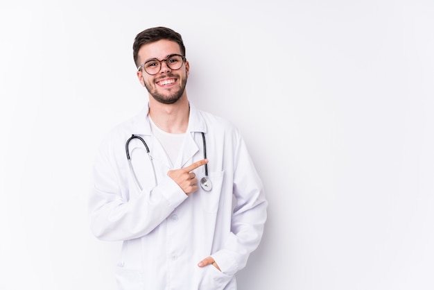 Homem jovem médico caucasiano isolado sorrindo e apontando de lado, mostrando algo no espaço em branco.