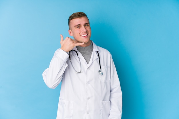 Homem jovem médico caucasiano mostrando um gesto de chamada de celular com os dedos.