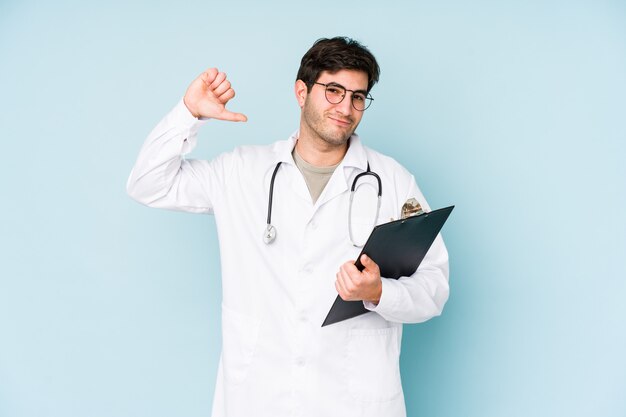 Homem jovem médico isolado no azul sente orgulho e auto-confiança, exemplo a seguir.