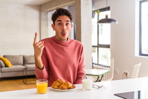 Foto homem jovem mestiço tomando café da manhã em uma cozinha pela manhã, tendo uma ótima ideia, o conceito de criatividade.