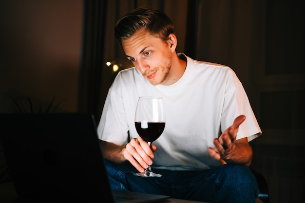 Foto homem jovem milenar com videochamada no computador laptop e bebendo vinho, usa a tecnologia para se comunicar com amigos ou família.