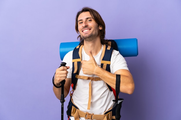 Homem jovem montanhista com uma grande mochila sobre uma parede isolada fazendo um gesto de polegar para cima