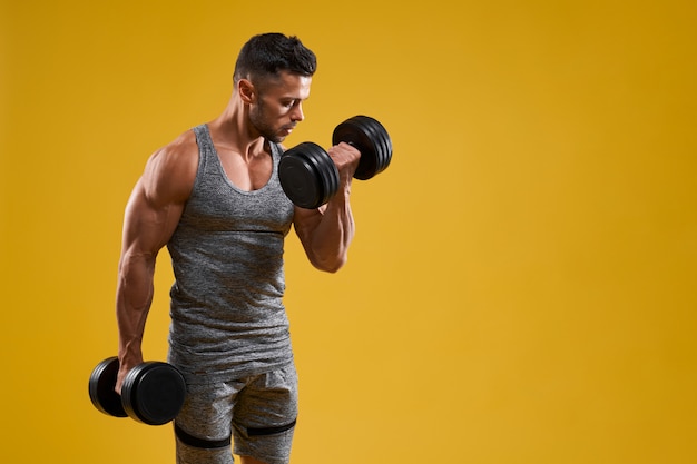 Homem jovem musculoso fazendo exercício com halteres