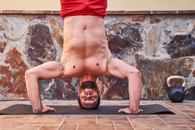 Homem jovem musculoso fazendo parada de mãos em casa. Conceito de treino em casa e vida saudável.