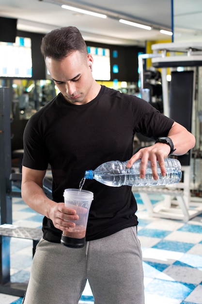 Foto homem jovem musculoso preparando shake de proteína.