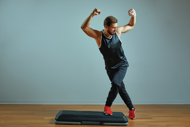 Homem jovem musculoso treinando em plataformas de etapa na parede cinza