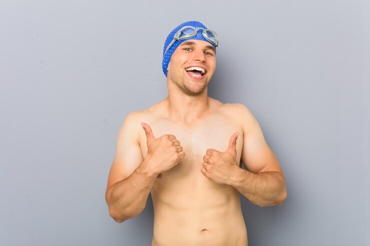 Foto homem jovem nadador profissional, levantando os dois polegares, sorrindo e confiante.