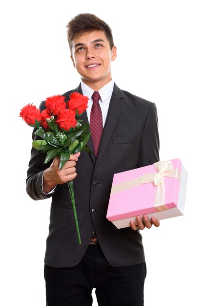 Homem jovem pensativo feliz sorrindo enquanto segura o buquê de rosas vermelhas e a caixa de presente rosa. Conceito de dia dos namorados