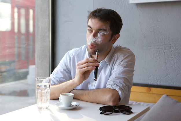 Homem jovem, sentando dentro, fumar, cigarro elétrico