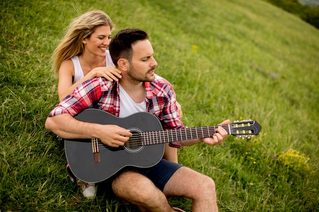 Homem jovem, sentar-se grama, com, seu, namorada, e, violão jogo