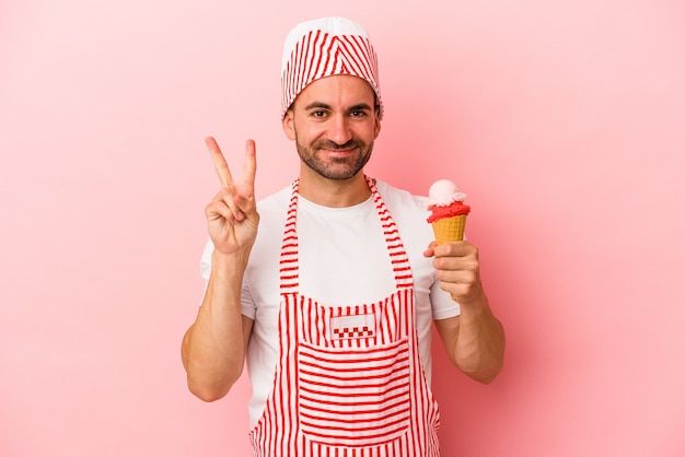 Foto homem jovem sorveteiro segurando sorvete isolado no fundo rosa, mostrando o número dois com os dedos.