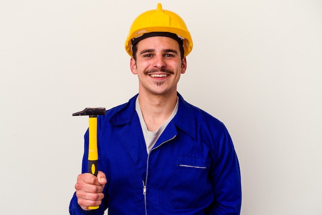 Homem jovem trabalhador caucasiano segurando um martelo isolado no fundo branco feliz, sorridente e alegre.