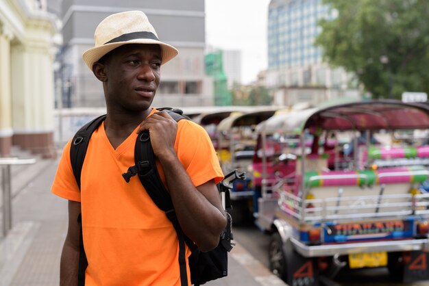 Homem jovem turista pensando enquanto segura a mochila e passear na estação ferroviária com triciclos em Bangkok Tailândia