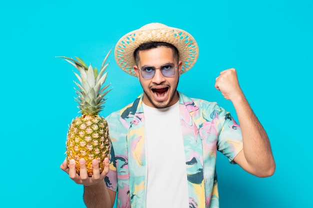 Homem jovem viajante hispânico celebrando uma vitória bem-sucedida e segurando um abacaxi