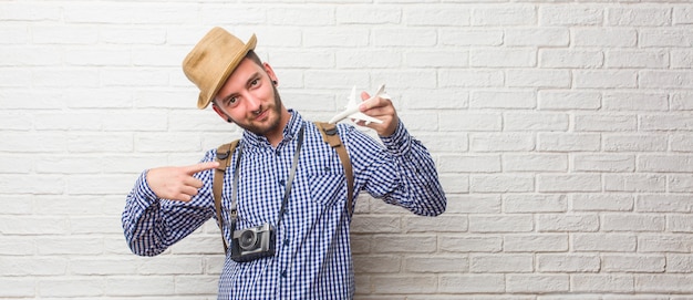 Homem jovem viajante usando mochila e uma câmera vintage orgulhosa e confiante, apontando os dedos