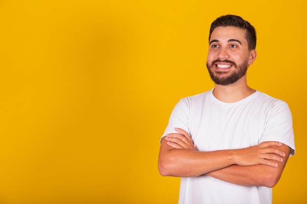 Homem latino-americano com braços cruzados sorrindo confiante e confiante espaço de cópia de fundo amarelo