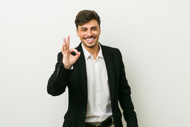 Homem latino-americano do negócio novo alegre e seguro mostrando o gesto aprovado.