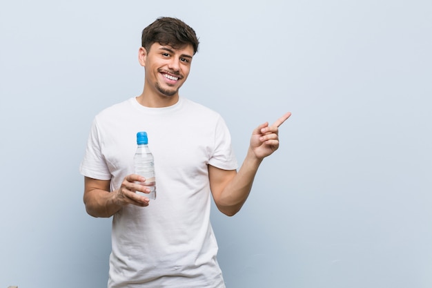 Homem latino-americano novo que guarda uma garrafa de água que sorri alegremente apontando com o dedo indicador afastado.