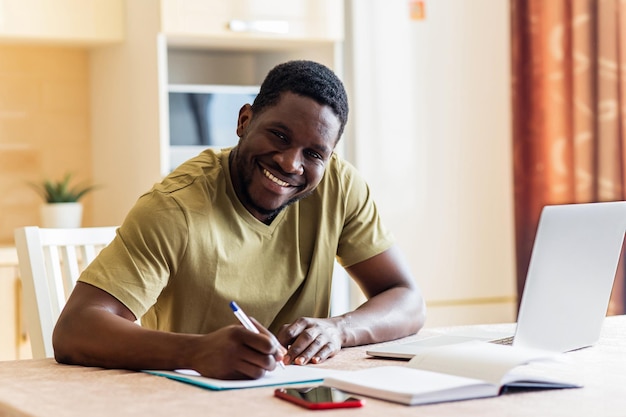 Homem latino-americano parecendo feliz enquanto está sentado com o laptop e papéis na cozinha