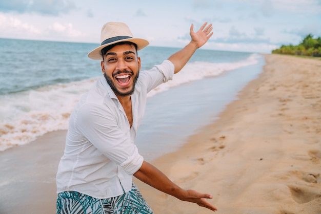 Homem latino-americano sorridente na praia apontando para o espaço à direita com a palma da mão