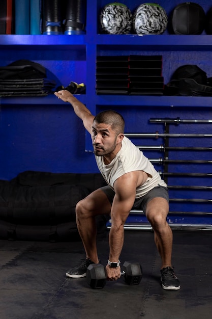 Homem latino com roupas esportivas fazendo exercícios com halteres no ginásio