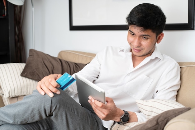 Homem latino com tablet e cartão de crédito comprando online no sofá