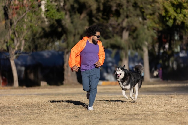 Foto homem latino correndo em um parque com seu cão husky atrás dele conceito de dia de animais de estimação