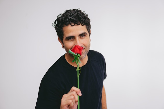 Homem latino de meia-idade cheirando uma rosa enquanto olha para a câmera em um fundo branco