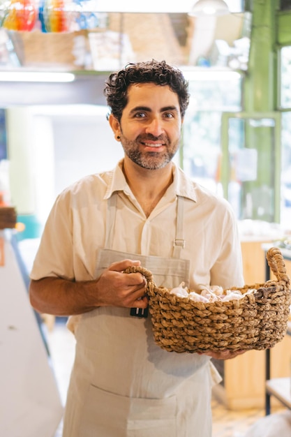 Homem latino de meia-idade olhando para a câmera usando um avental enquanto sorria e carregava uma cesta de vime