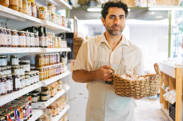 Homem latino de meia-idade segurando uma cesta de vime em uma loja de produtos orgânicos enquanto olha para a câmera