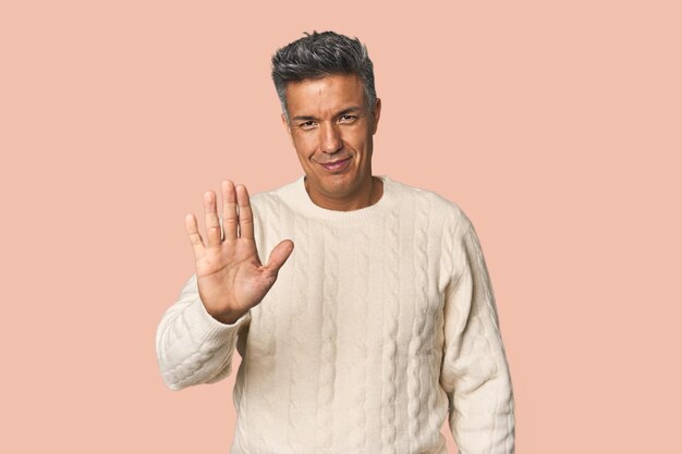 Homem latino de meia-idade sorrindo alegremente mostrando o número cinco com os dedos