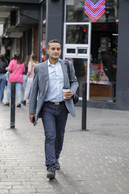 Homem latino de terno com uma xícara de café descartável na mão atravessando a rua em uma cidade