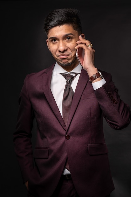 Foto homem latino de terno em fundo preto falando ao telefone, olhando para a câmera