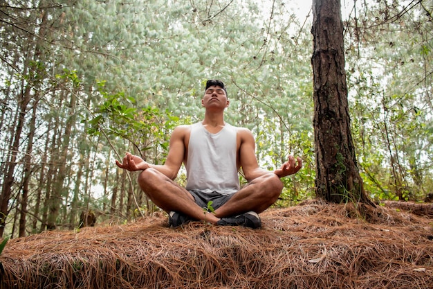 Homem latino fazendo ioga na natureza Estilo de vida saudável na natureza Jovem adulto meditando no meio de árvores e ar fresco