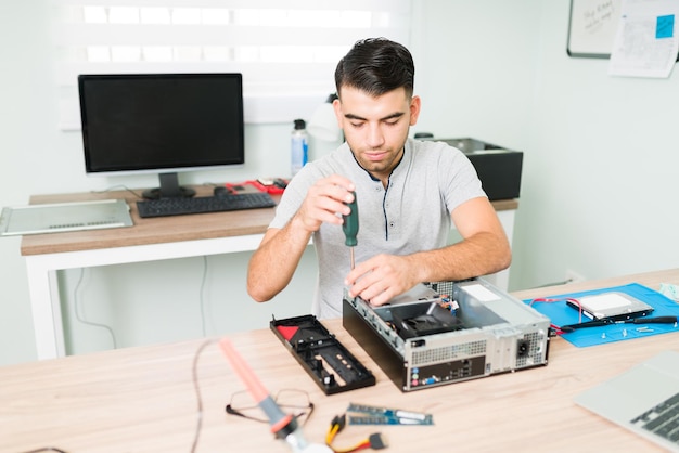 Homem latino focado usando uma chave de fenda para desmontar os componentes de um computador cpu. técnico masculino trabalhando na reparação de hardware