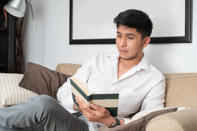 Homem latino lendo livro no sofá