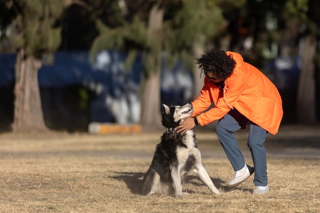 Foto homem latino mexicano com cabelo encaracolado acariciando com seu cão husky em um parque