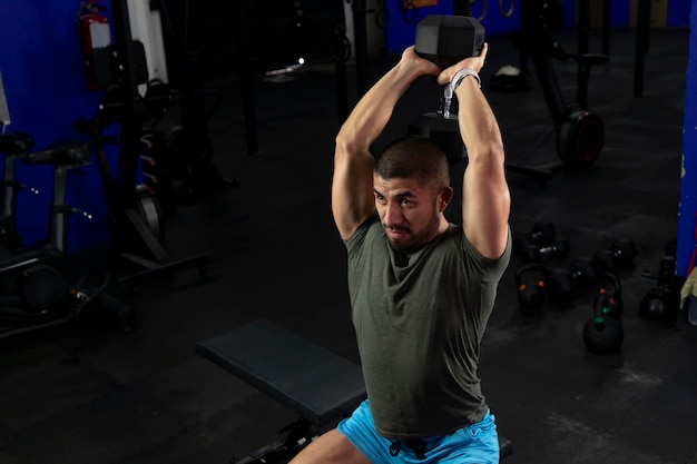 Homem latino musculoso fazendo exercícios para bíceps sentado em um banco de ginástica