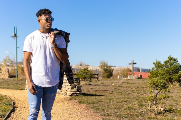 Homem latino negro andando por um parque na rua no verão com uma jaqueta por cima do ombro Retrato vertical