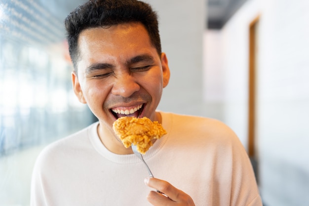 Homem latino sorrindo e segurando o garfo com frango frito para comer