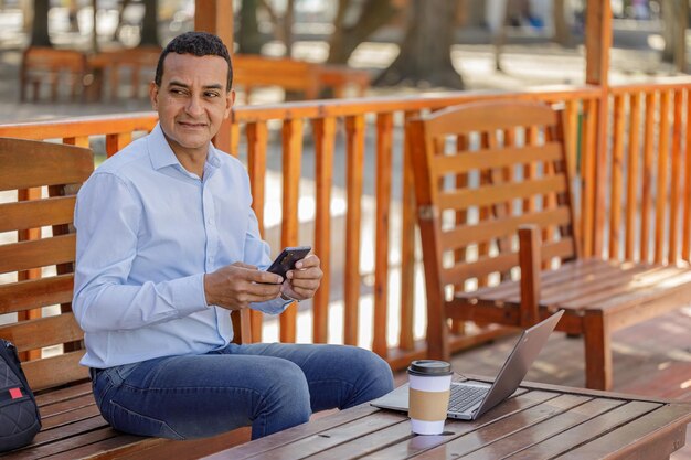 Homem latino usando um laptop enquanto toma café em um bar ao ar livre