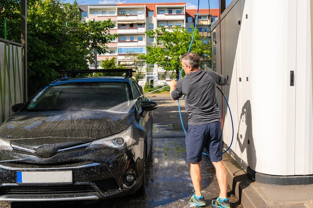 Homem lava seu carro com água e sabão na lavagem de carros de autoatendimento O foco é no cuidado do carro, mantendo o carro limpo e cuidando de sua aparência.