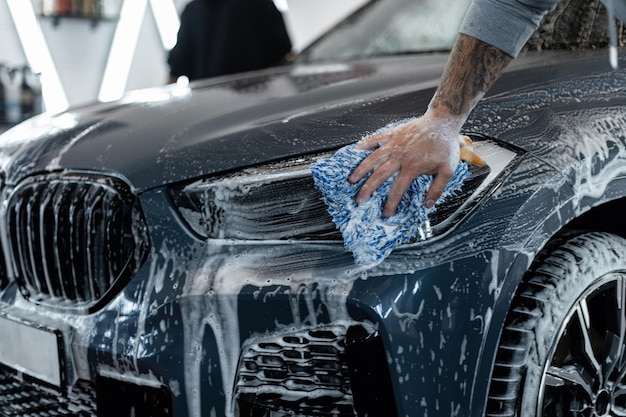 Homem lavador de carros profissional lava carros com espuma na garagem Lavagem de carros e detalhamento