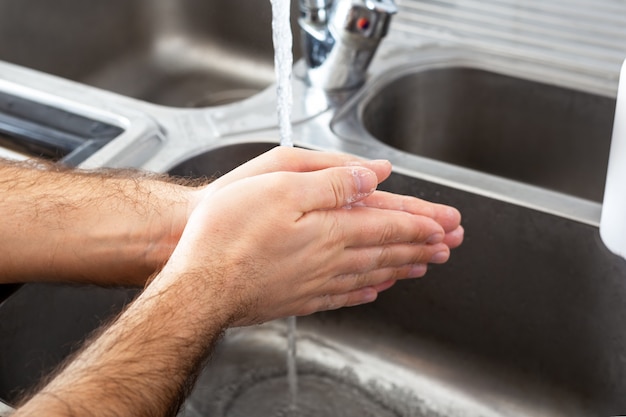 Homem lavando as mãos com água e sabão antibacteriano em pia de metal para prevenção de vírus corona.